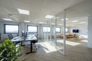 Modern en licht kantoorinterieur aan de Joan Muyskenweg met open werkplekken, glazen vergaderruimte en houten vergadertafel.